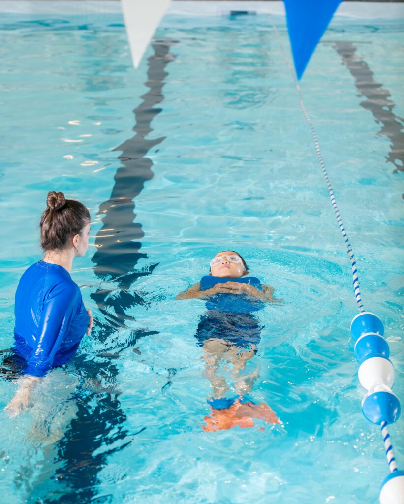 A swimming instructor teaches a young child to swim in an indoor pool.